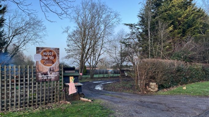 Entrance to a rural area with a sign, trees, and a clear blue sky.