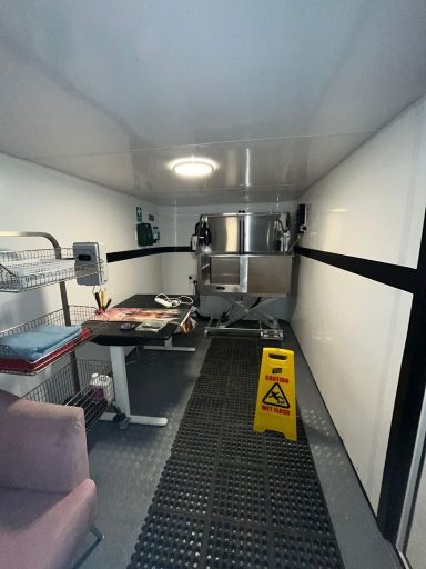 Interior of a trailer with equipment, a chair, and a "wet floor" caution sign.