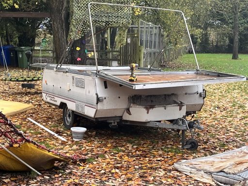 A weathered camping trailer in a leafy outdoor setting.